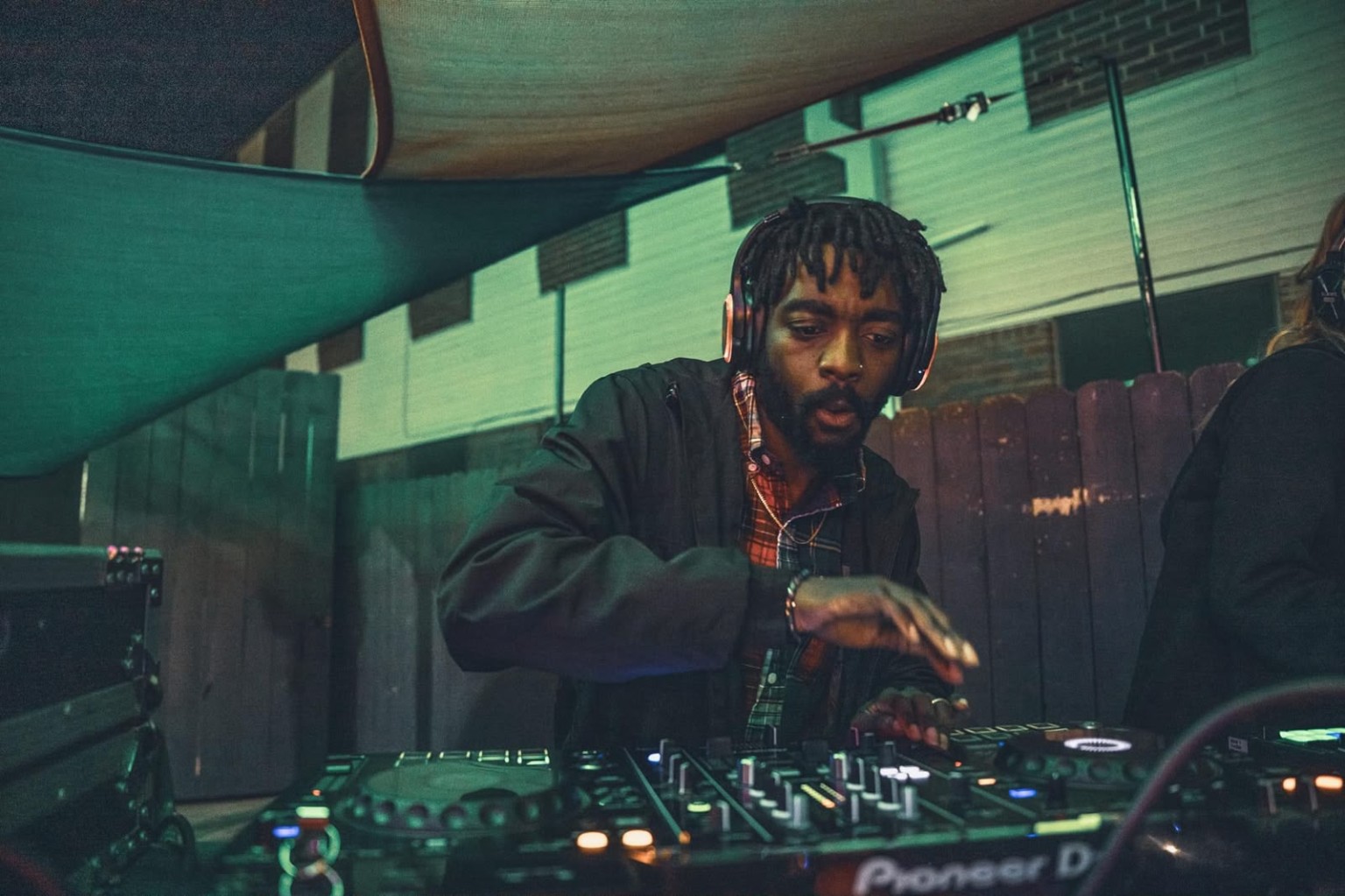 DJ MalkyyWayy in a black jacket, wearing headphones and mixing music at his DJ controller